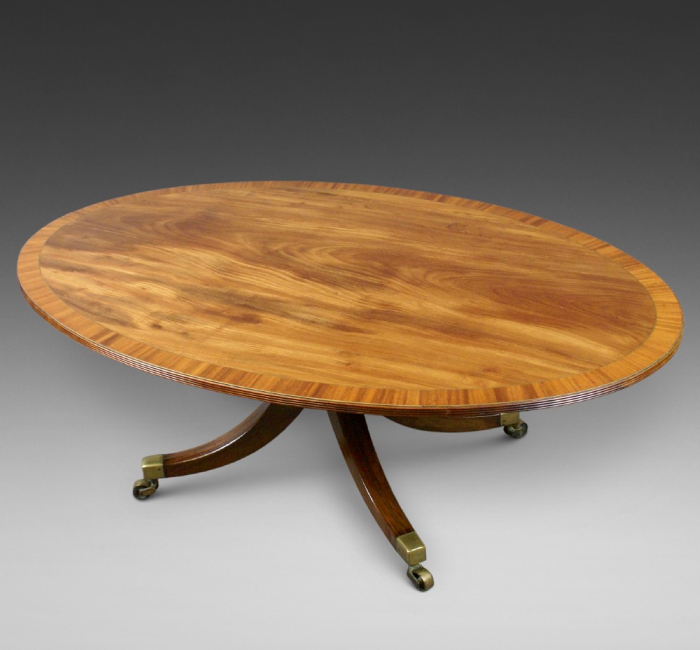 An oval flame mahogany coffee table with a crossbanded border resting on four splayed legs fitted with brass castors.