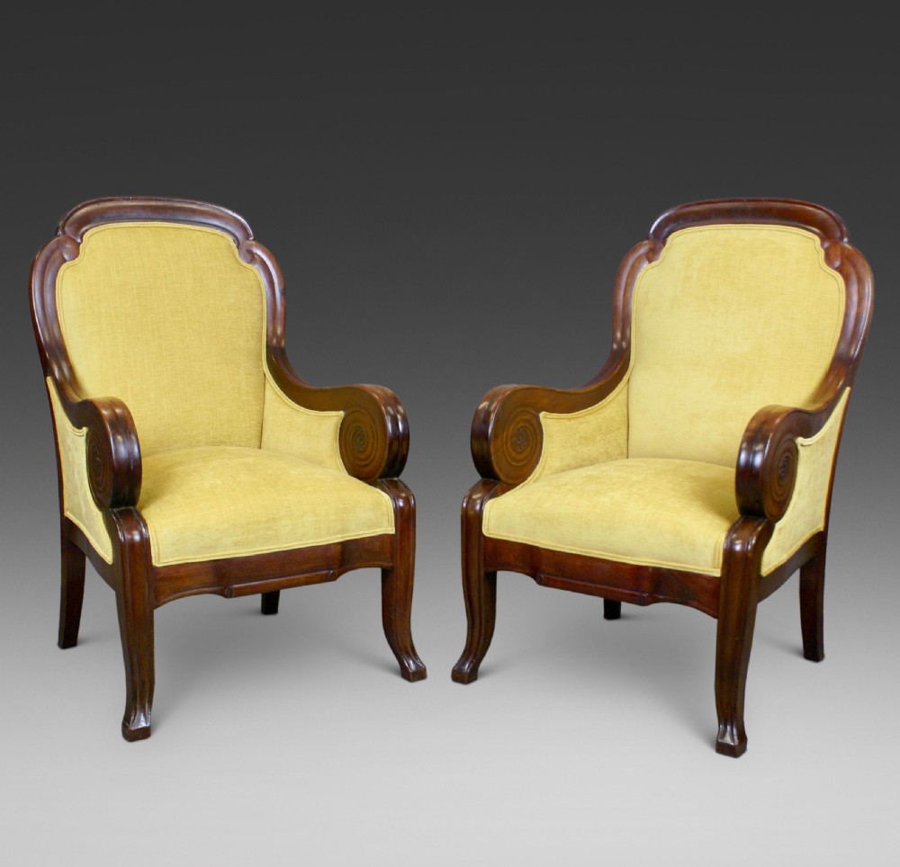 A pair of antique mahogany library armchairs featuring bold scroll arms and yellow fabric upholstery.