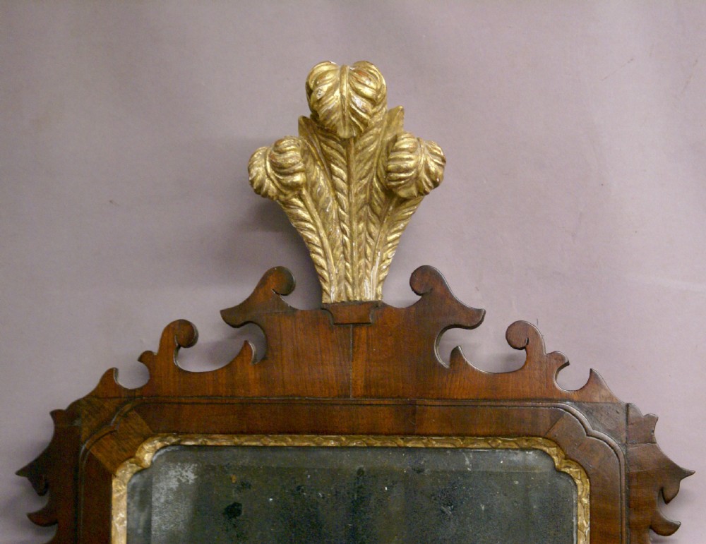 An 18th-century rectangular mahogany wall mirror featuring carved parcel-gilt mouldings, side floral garlands, a scrolled fretwork apron, and a leaf finial cresting. View II