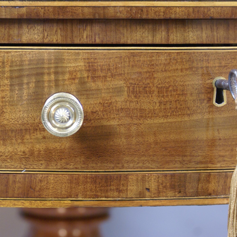 A circular Georgian mahogany drum table with an inset leather top, perimeter frieze drawers with brass knobs, and a turned pedestal on four splayed legs with brass castors. View II