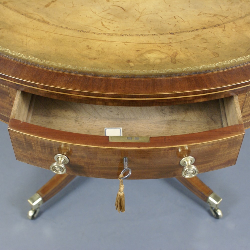 A circular Georgian mahogany drum table with an inset leather top, perimeter frieze drawers with brass knobs, and a turned pedestal on four splayed legs with brass castors. View VII