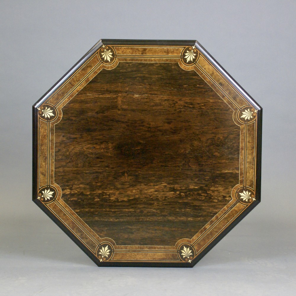 An octagonal dark rosewood occasional table featuring foliate marquetry inlays around the border, turned supports, a cross-stretcher, and splayed legs with brass castors. View II