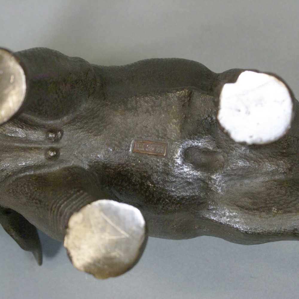 A dark brown patinated bronze elephant sculpture in mid-stride with light-coloured tusks and detailed skin texture. View VII