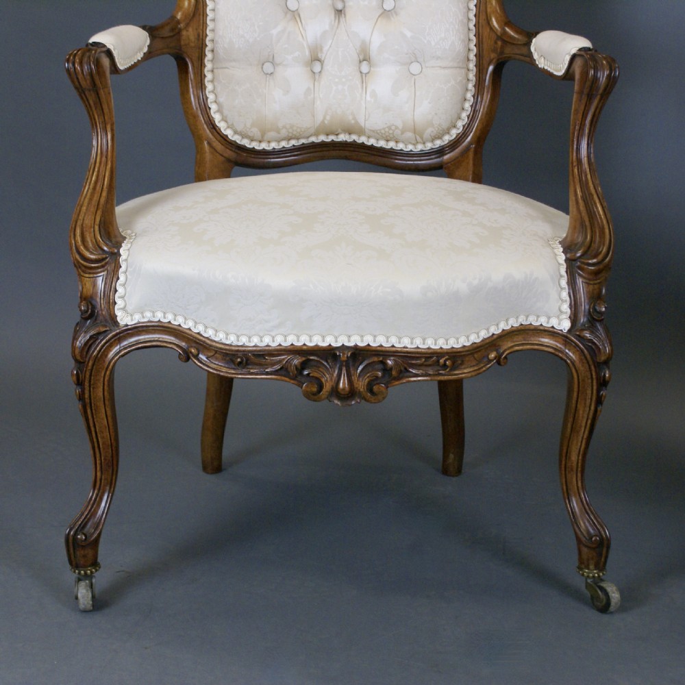 A pair of Victorian carved rosewood open armchairs with button-tufted cream upholstery and cabriole legs on brass castors. View II