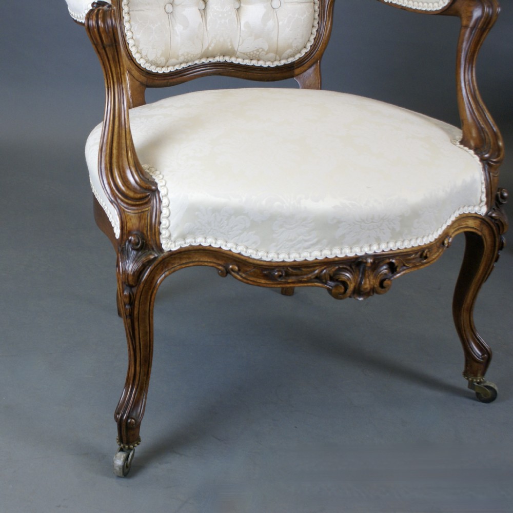 A pair of Victorian carved rosewood open armchairs with button-tufted cream upholstery and cabriole legs on brass castors. View IV