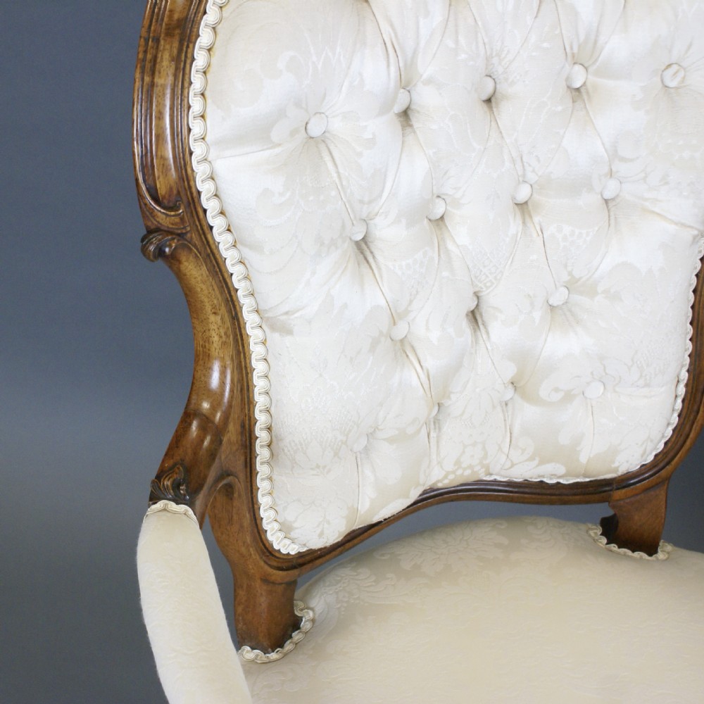 A pair of Victorian carved rosewood open armchairs with button-tufted cream upholstery and cabriole legs on brass castors. View V