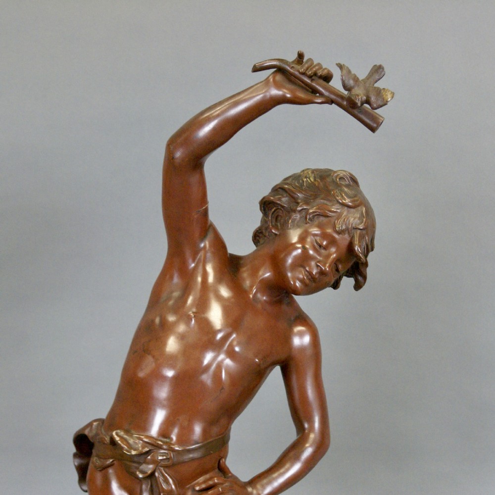 A warm brown patinated bronze figure of a youth reaching upward toward a bird perched on a branch, set on a naturalistic base. View III