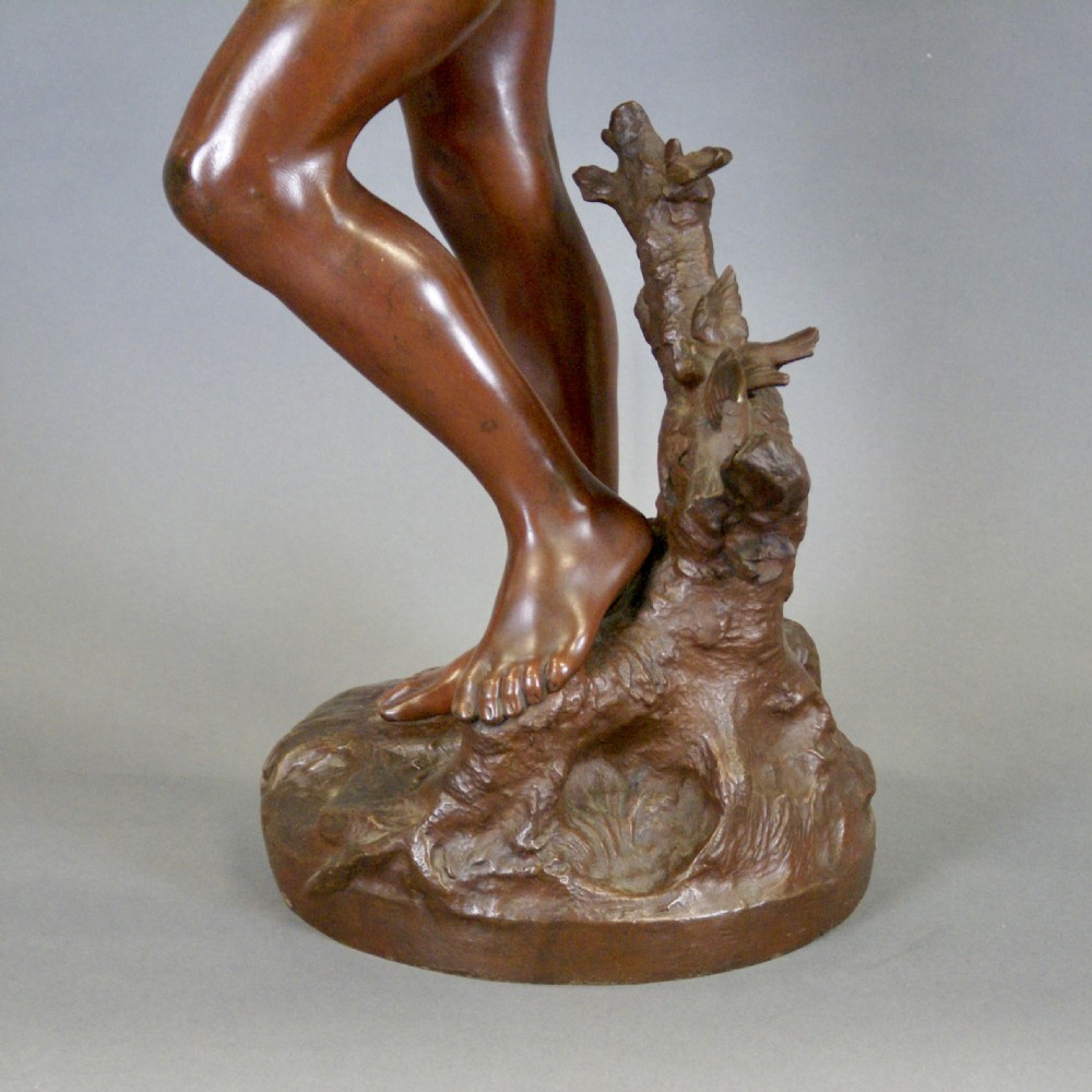 A warm brown patinated bronze figure of a youth reaching upward toward a bird perched on a branch, set on a naturalistic base. View VI
