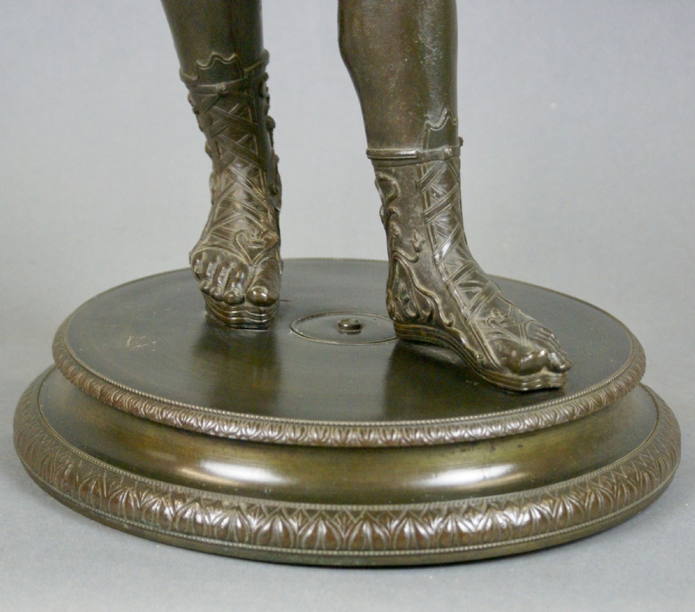 A patinated dark bronze classical figure of a youthful male deity standing on a circular moulded base. View VI