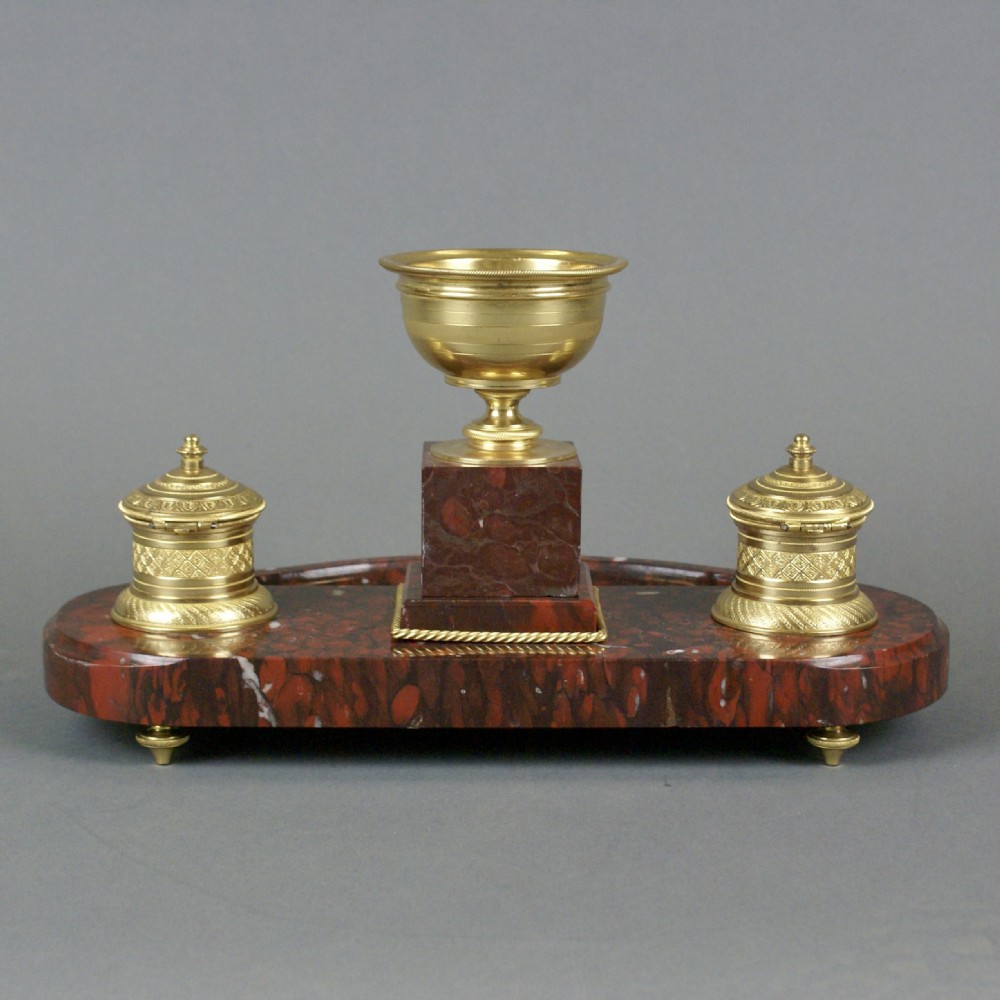 A French Neoclassical red marble inkstand featuring a central gilt urn on a pedestal decorated with a laurel wreath, flanked by two matching gilt inkwells. View V