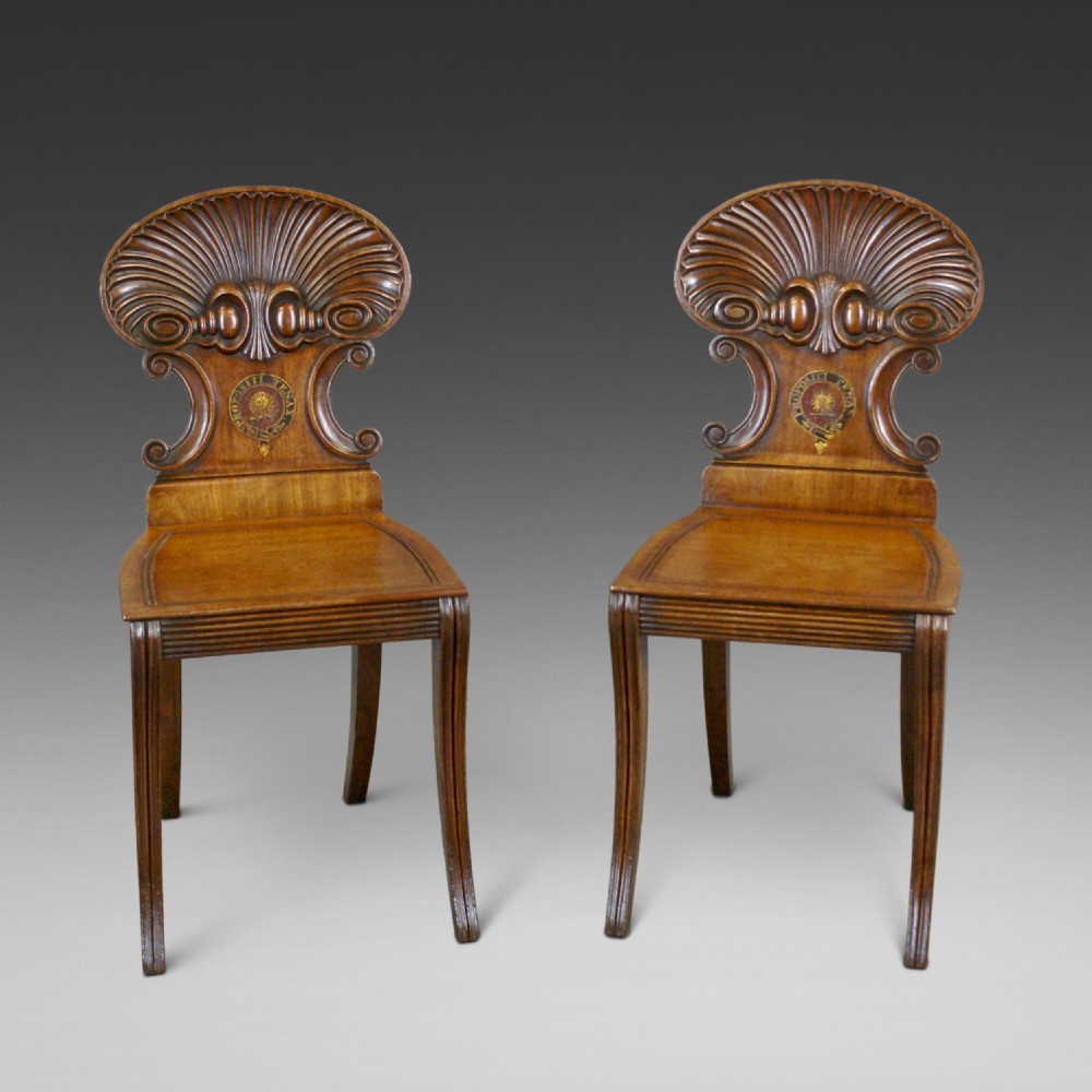 A pair of carved mahogany hall chairs featuring scalloped shell backs with painted crests and reeded front legs.