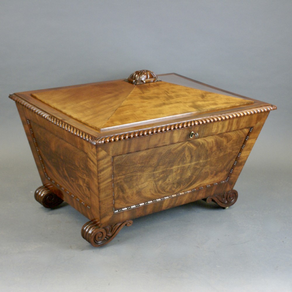 An antique Regency flame mahogany sarcophagus-shaped wine cooler featuring a pyramidal lid with carved finial, gadrooned borders, and scroll feet. View III
