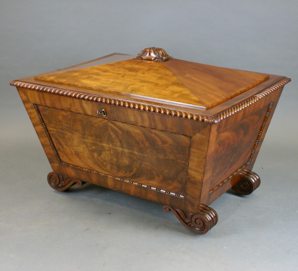 An antique Regency flame mahogany sarcophagus-shaped wine cooler featuring a pyramidal lid with carved finial, gadrooned borders, and scroll feet. View VIII