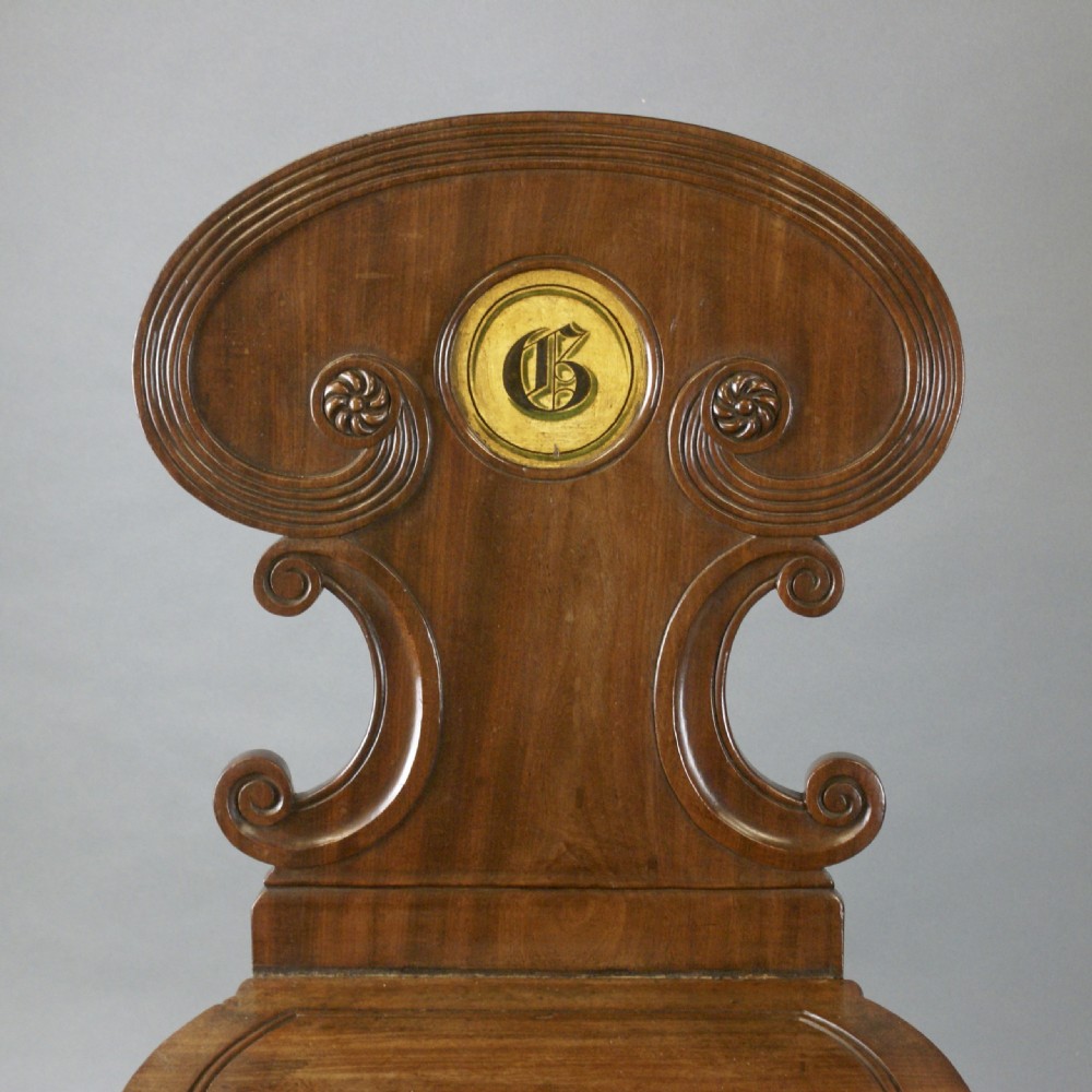 A pair of Regency mahogany hall chairs featuring carved cartouche backs with painted crest roundels, reeded seat rails, and sabre front legs. View III