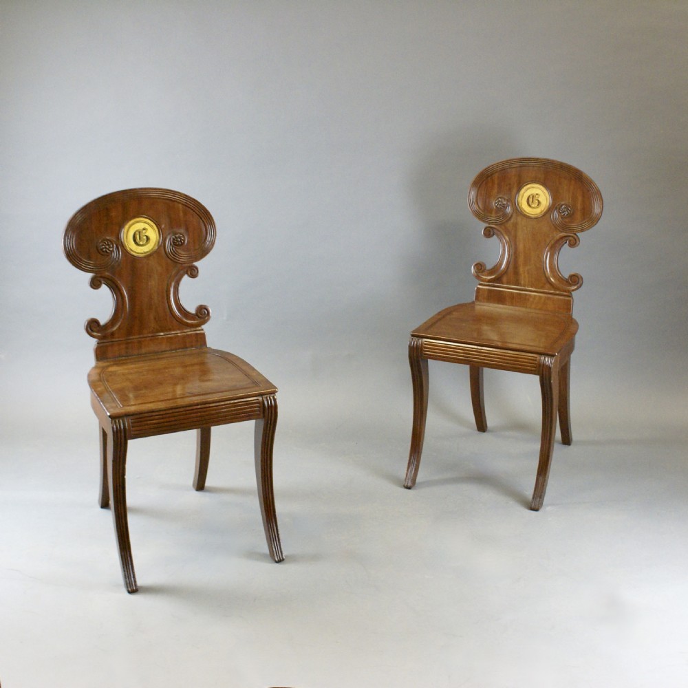 A pair of Regency mahogany hall chairs featuring carved cartouche backs with painted crest roundels, reeded seat rails, and sabre front legs. View IV