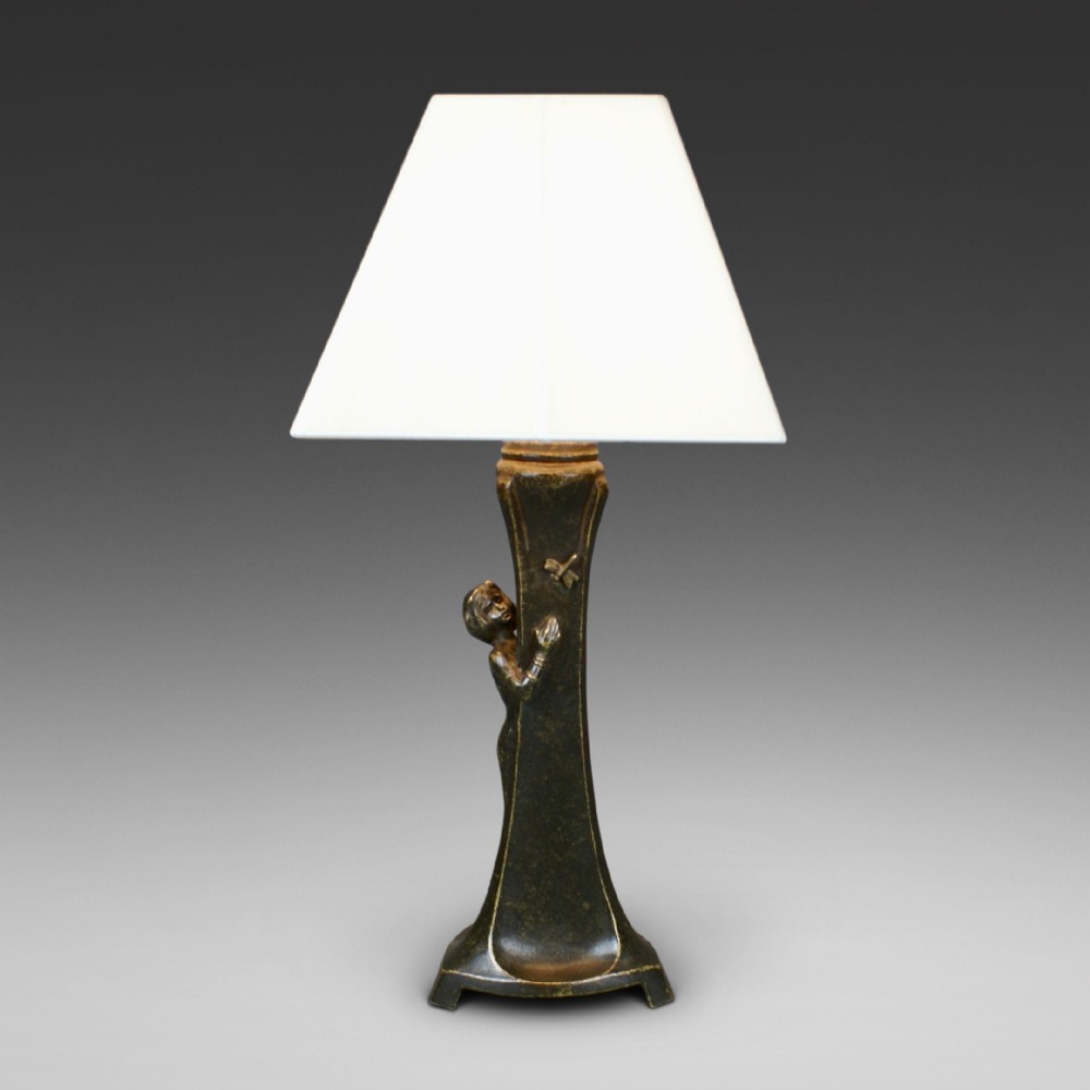 An Art Nouveau patinated bronze table lamp featuring a sculptural figure reaching towards a dragonfly on a flared stem, topped with a white conical shade.