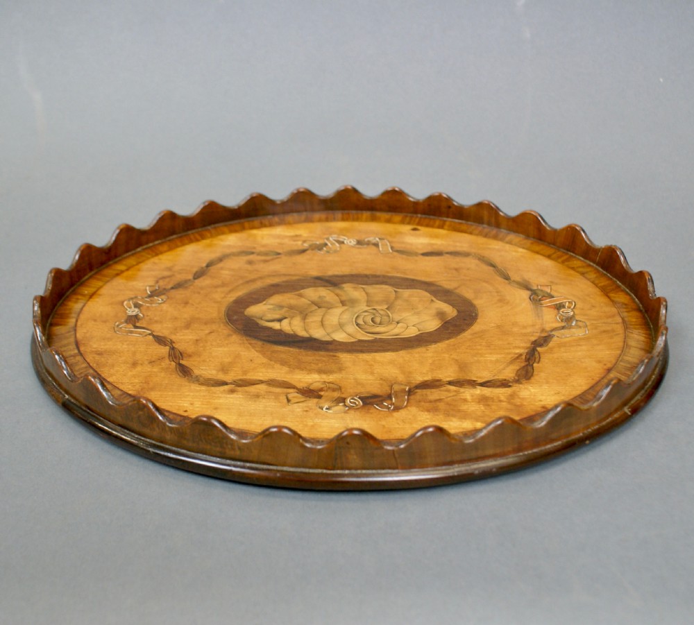 A miniature oval wooden tray featuring a central shell marquetry medallion surrounded by ribbon garland inlays and a wavy scalloped rim. View II