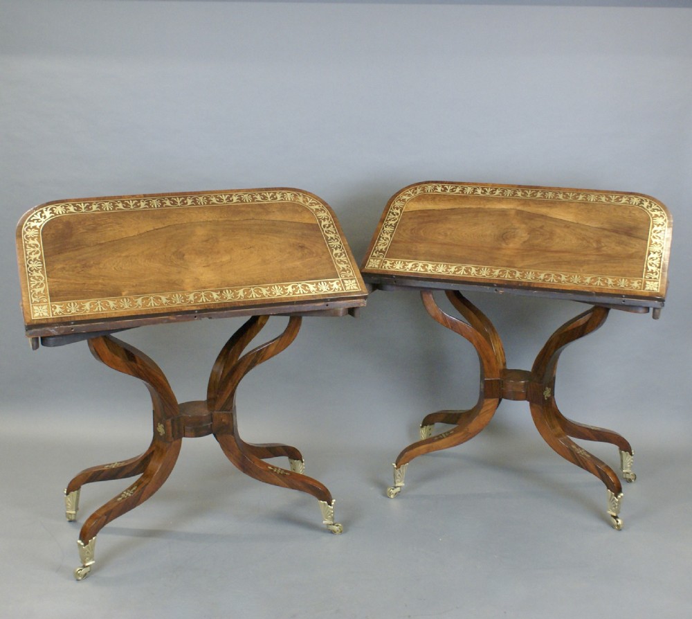 A pair of Regency dark rosewood card tables featuring fold-over rectangular tops decorated with brass floral inlays on curved sweeping legs with brass castors. View V
