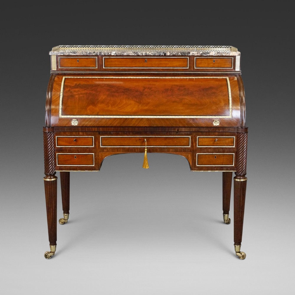 A Regency mahogany cylinder desk featuring a marble top with a brass gallery, brass-inlaid drawers, reeded tapered legs, and brass castors.