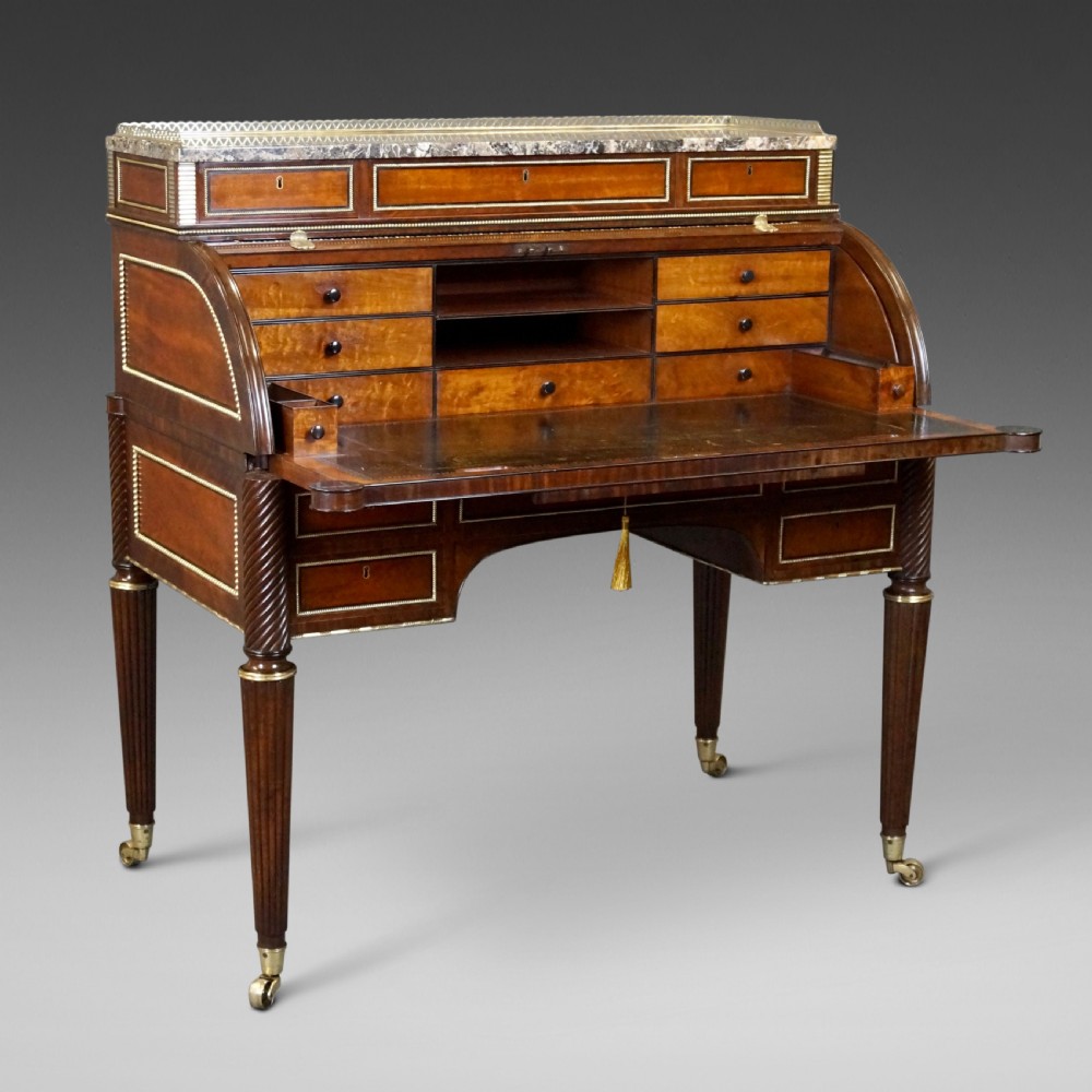A Regency mahogany cylinder desk featuring a marble top with a brass gallery, brass-inlaid drawers, reeded tapered legs, and brass castors. View II