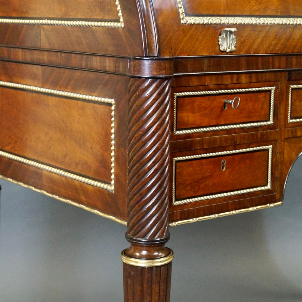 A Regency mahogany cylinder desk featuring a marble top with a brass gallery, brass-inlaid drawers, reeded tapered legs, and brass castors. View VI