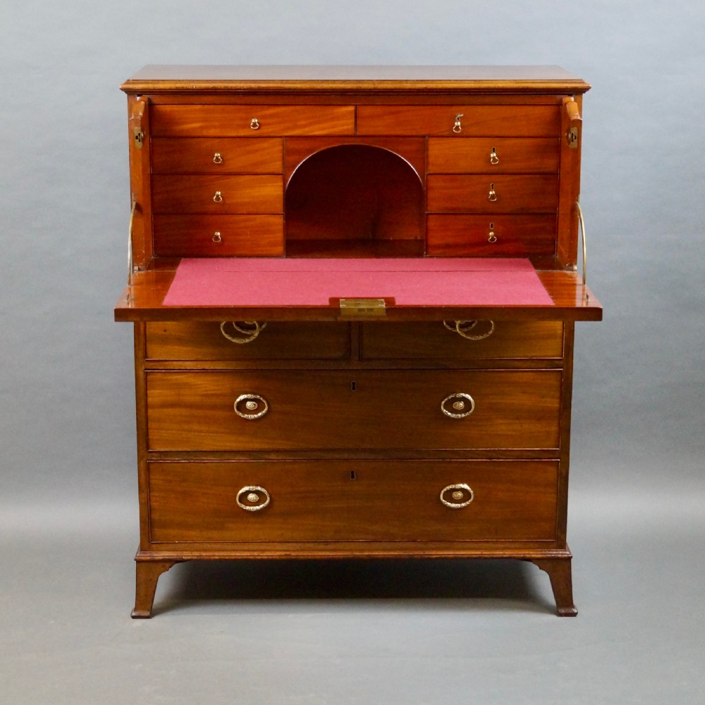 An antique mahogany secretaire chest of drawers featuring brass oval backplate handles, cockbeaded drawer edges, and bracket feet. View V