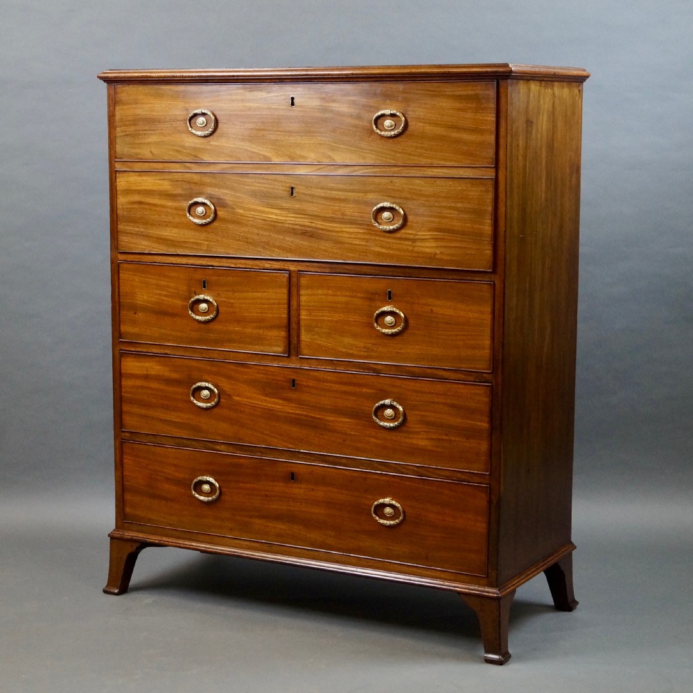 An antique mahogany secretaire chest of drawers featuring brass oval backplate handles, cockbeaded drawer edges, and bracket feet. View VI