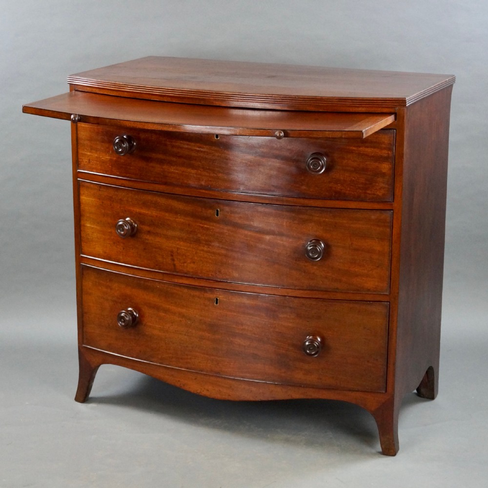 A George III bow-fronted mahogany chest featuring three graduated long drawers with turned wooden knobs and bracket feet. View II