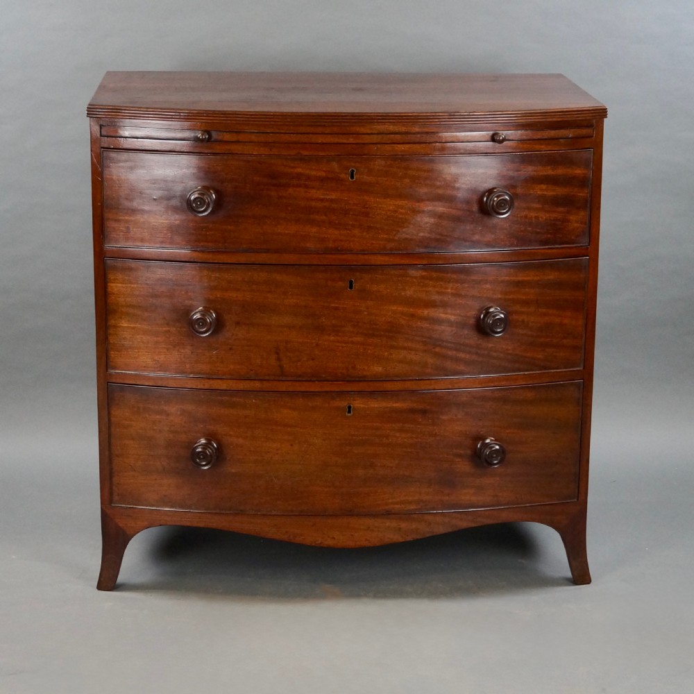 A George III bow-fronted mahogany chest featuring three graduated long drawers with turned wooden knobs and bracket feet. View V