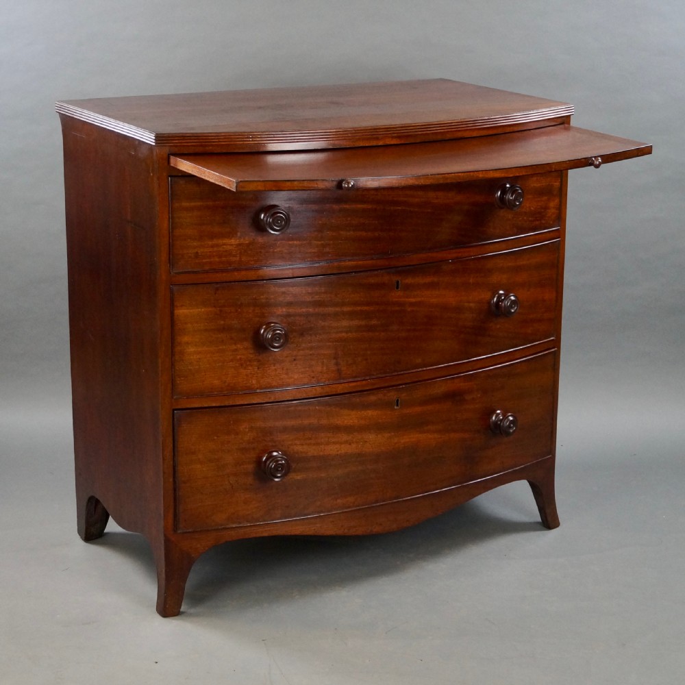 A George III bow-fronted mahogany chest featuring three graduated long drawers with turned wooden knobs and bracket feet. View VI
