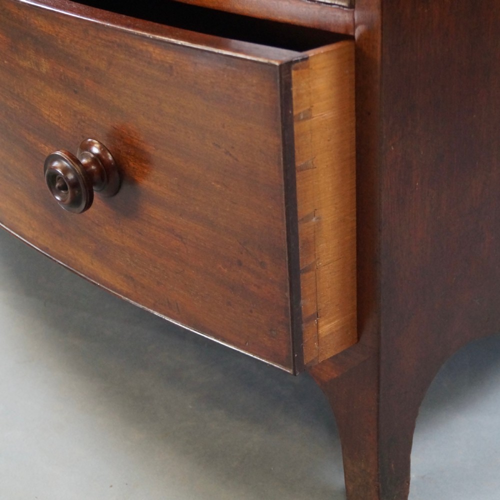 A George III bow-fronted mahogany chest featuring three graduated long drawers with turned wooden knobs and bracket feet. View VII