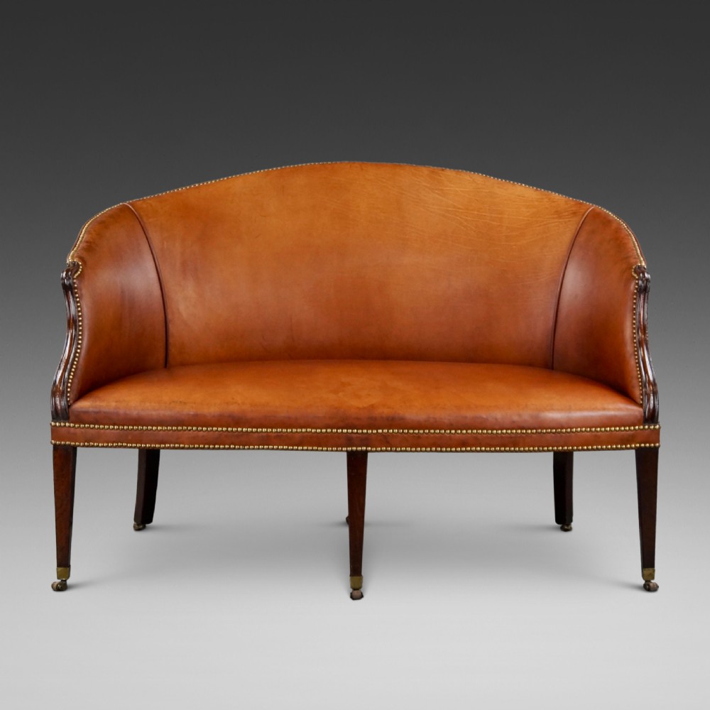 An 18th-century Hepplewhite period sofa upholstered in tan leather with brass stud trimming and tapered mahogany legs on brass castors.