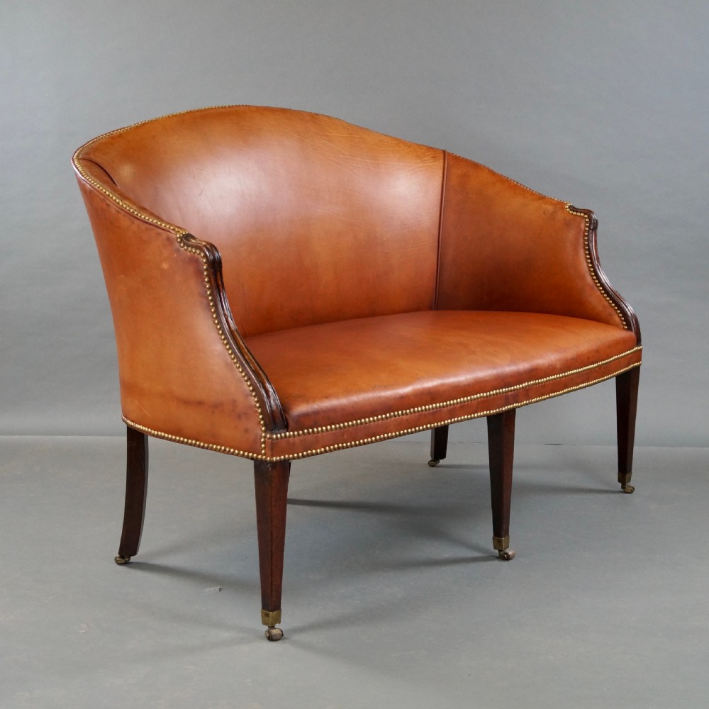 An 18th-century Hepplewhite period sofa upholstered in tan leather with brass stud trimming and tapered mahogany legs on brass castors. View II