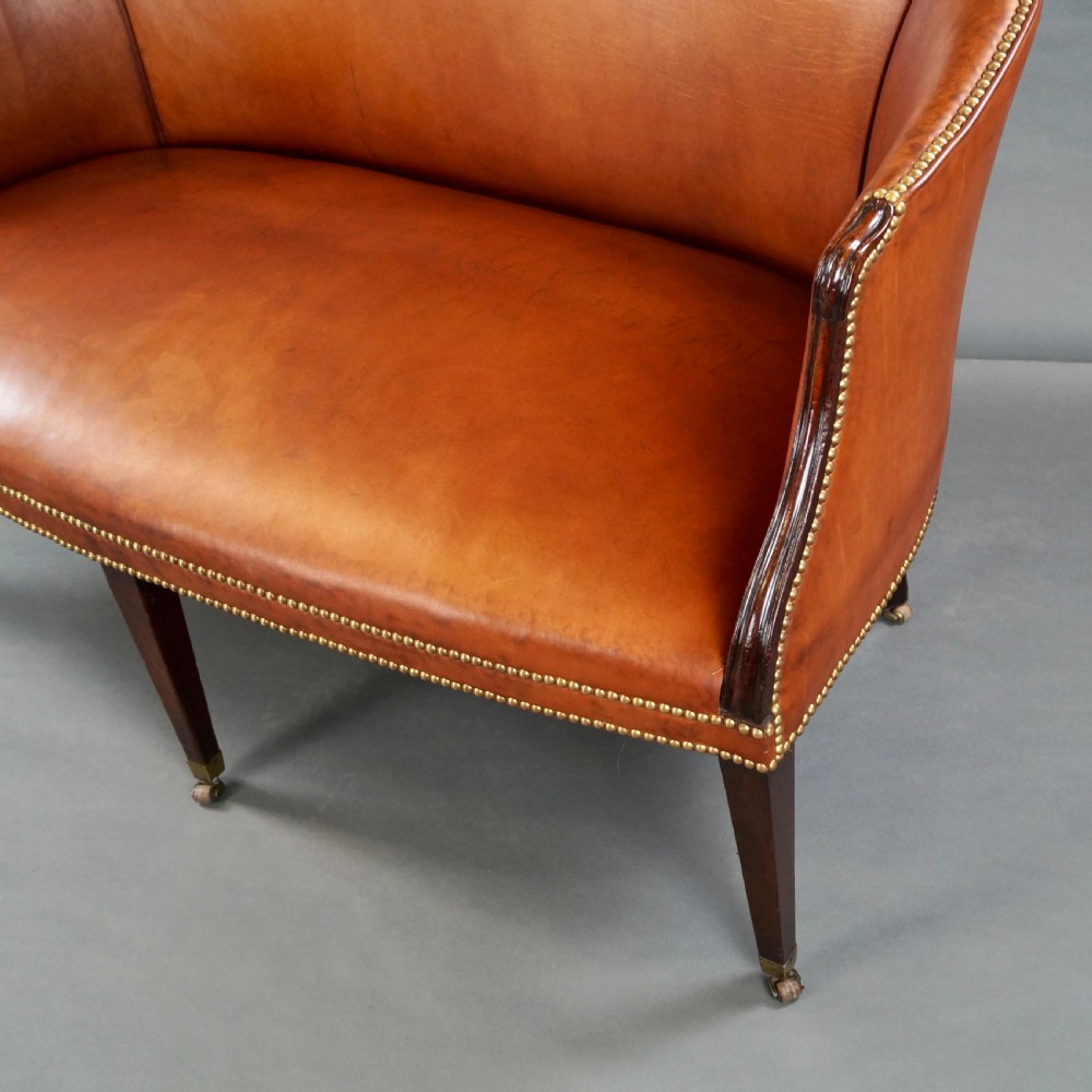 An 18th-century Hepplewhite period sofa upholstered in tan leather with brass stud trimming and tapered mahogany legs on brass castors. View III
