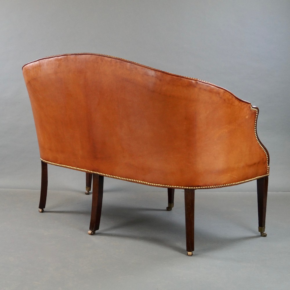 An 18th-century Hepplewhite period sofa upholstered in tan leather with brass stud trimming and tapered mahogany legs on brass castors. View V