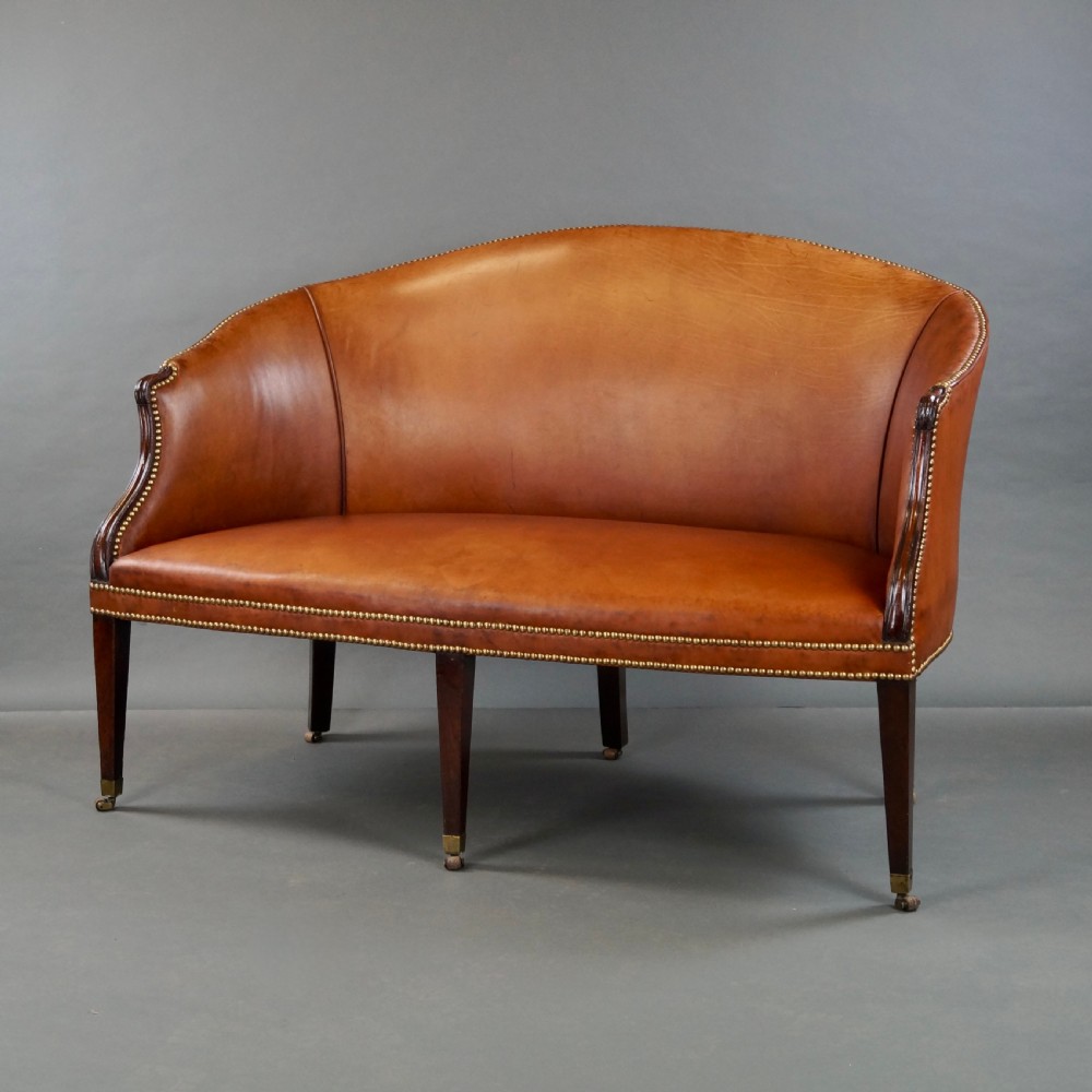 An 18th-century Hepplewhite period sofa upholstered in tan leather with brass stud trimming and tapered mahogany legs on brass castors. View VII