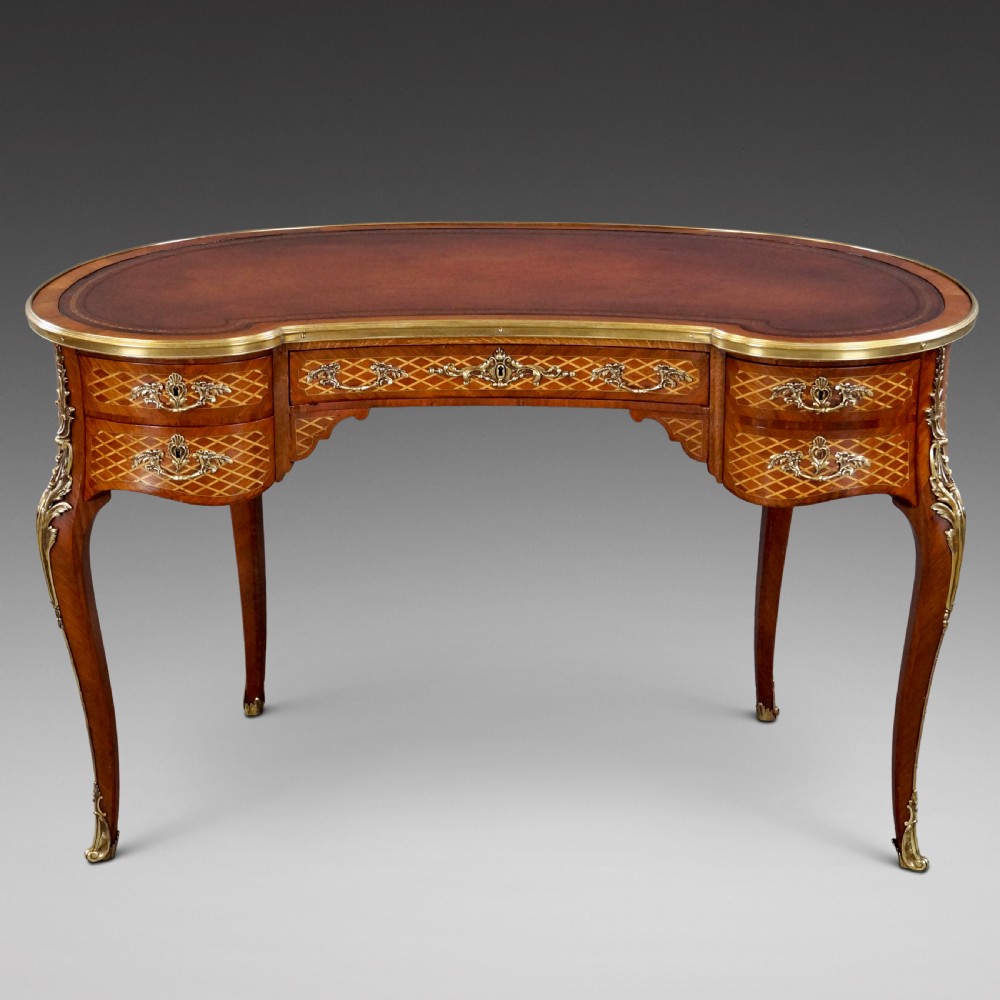 A French Louis XV style kidney-shaped writing desk featuring a brown leather top, parquetry veneer, gilded mounts, and cabriole legs.