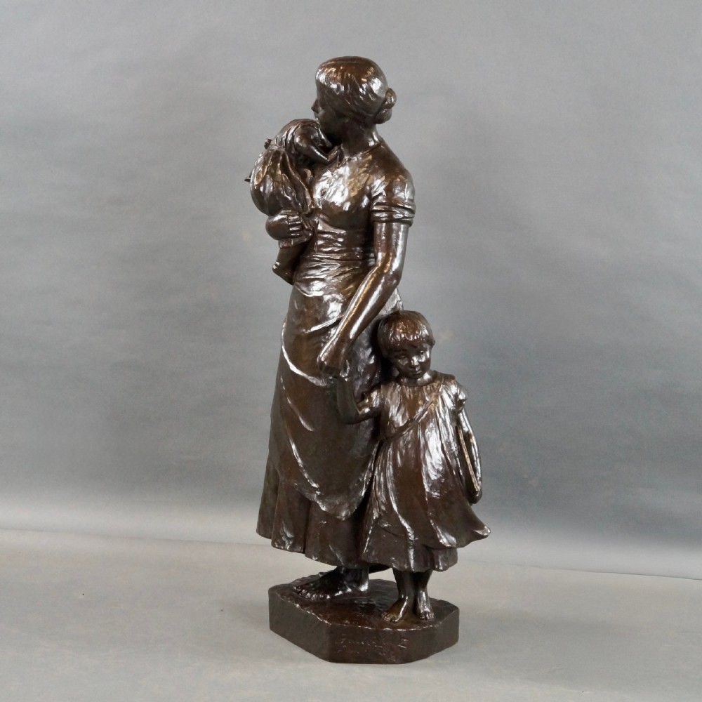 A dark brown patinated bronze figural sculpture depicting a standing mother holding an infant with a young child standing at her side. View III