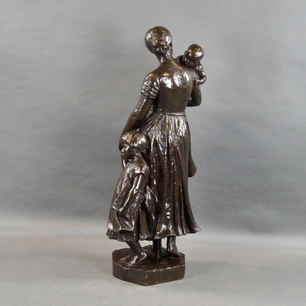 A dark brown patinated bronze figural sculpture depicting a standing mother holding an infant with a young child standing at her side. View V