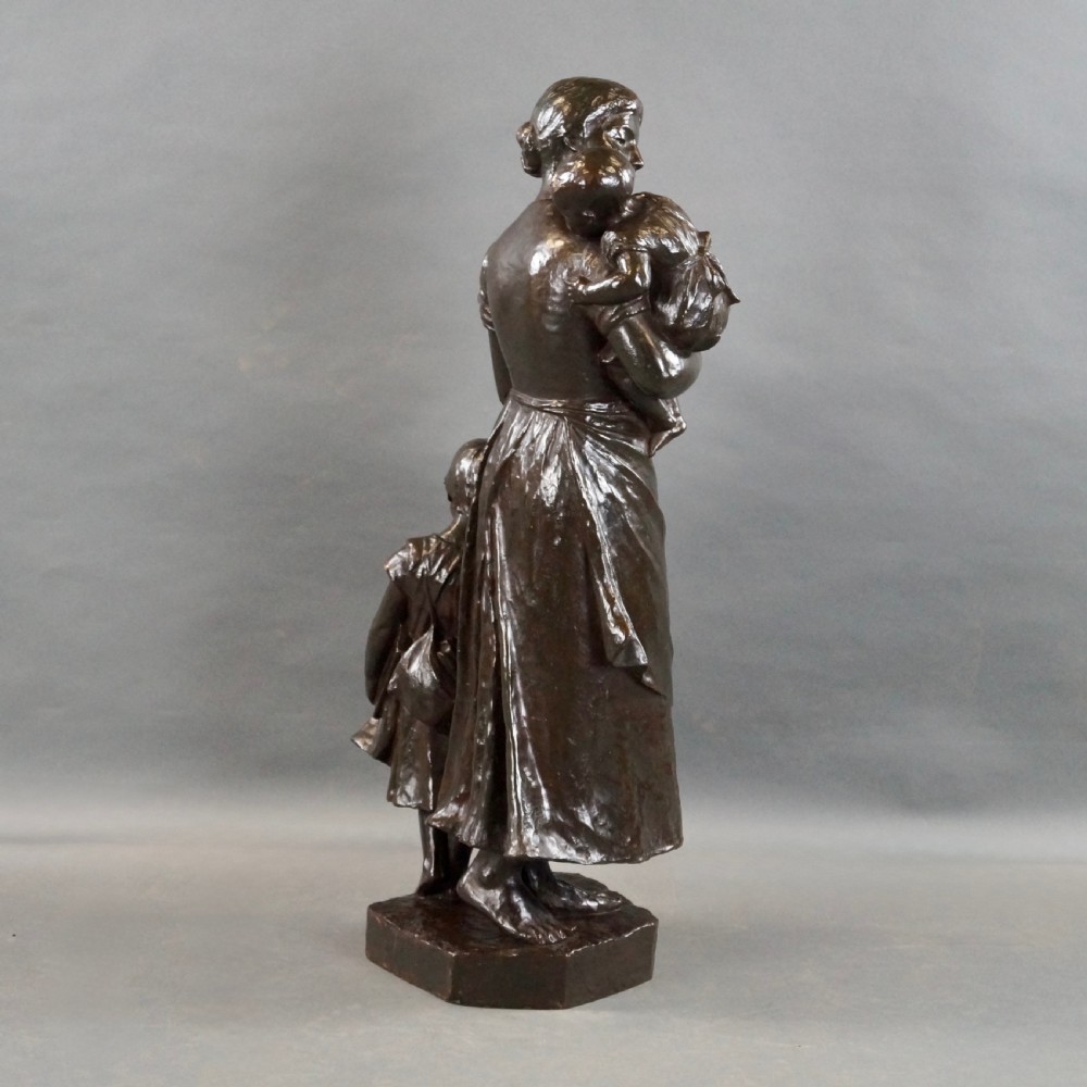 A dark brown patinated bronze figural sculpture depicting a standing mother holding an infant with a young child standing at her side. View VI