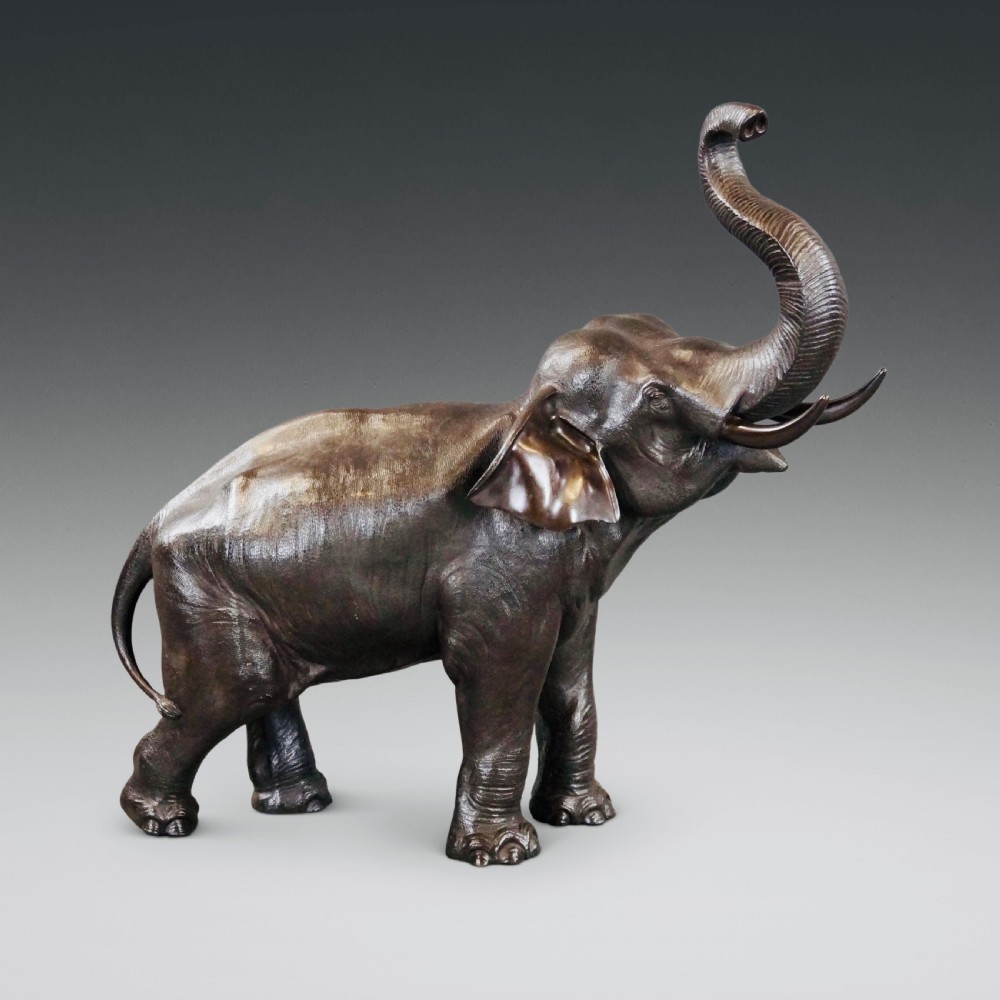 A cast bronze sculpture of an elephant standing with its trunk raised high, created in the Japanese Meiji style.