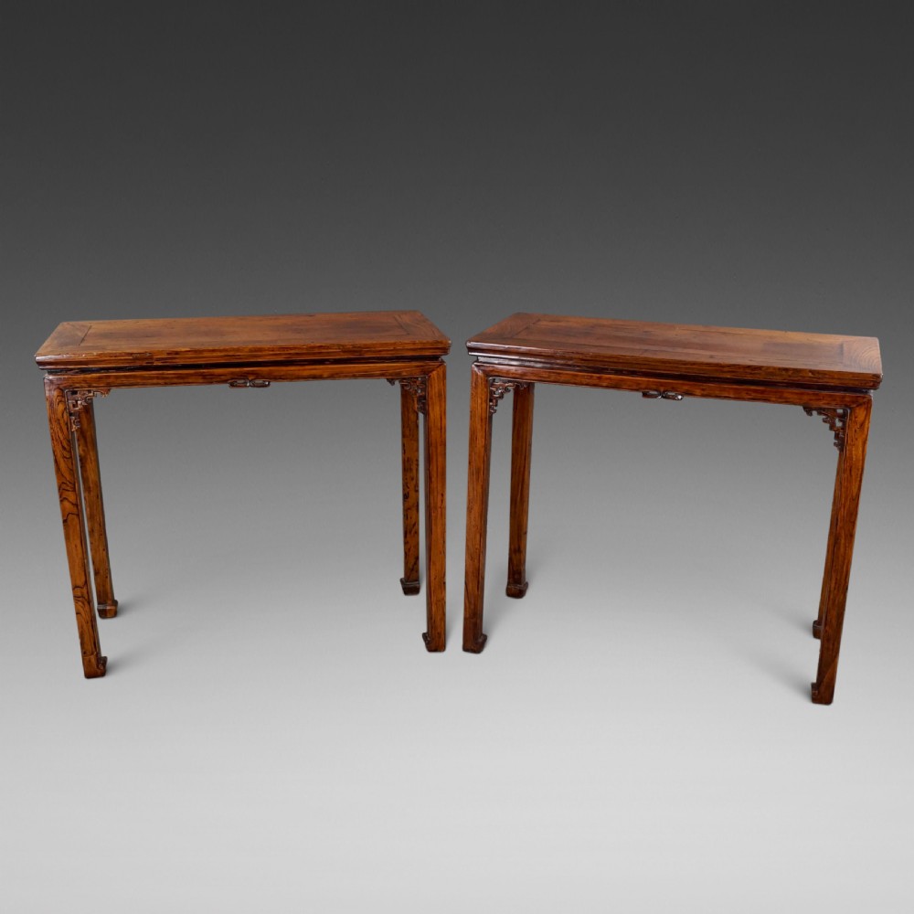 A pair of 19th-century Chinese elm side tables featuring rectangular floating panel tops, carved corner spandrels, and tall straight legs.