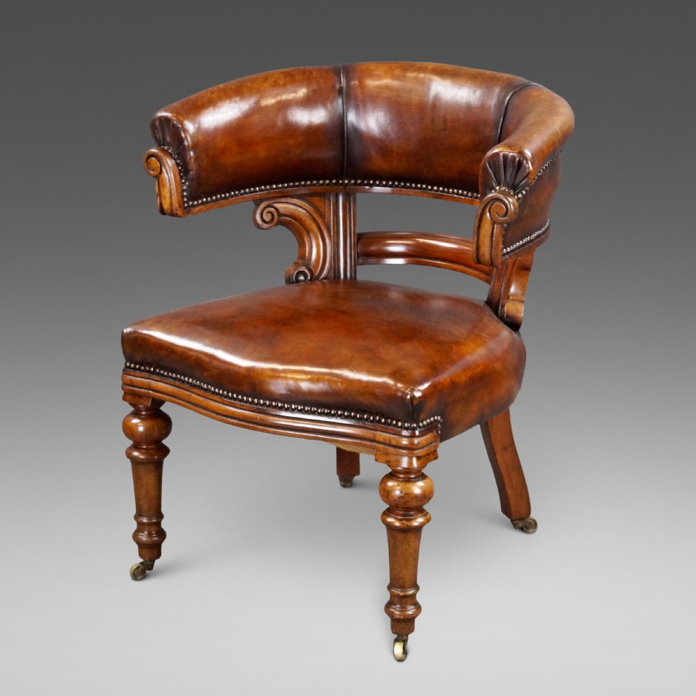 Victorian walnut desk chair upholstered in brown leather with brass stud detailing, carved scroll supports, and turned front legs on brass castors.