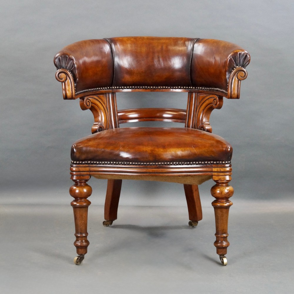 Victorian walnut desk chair upholstered in brown leather with brass stud detailing, carved scroll supports, and turned front legs on brass castors. View II