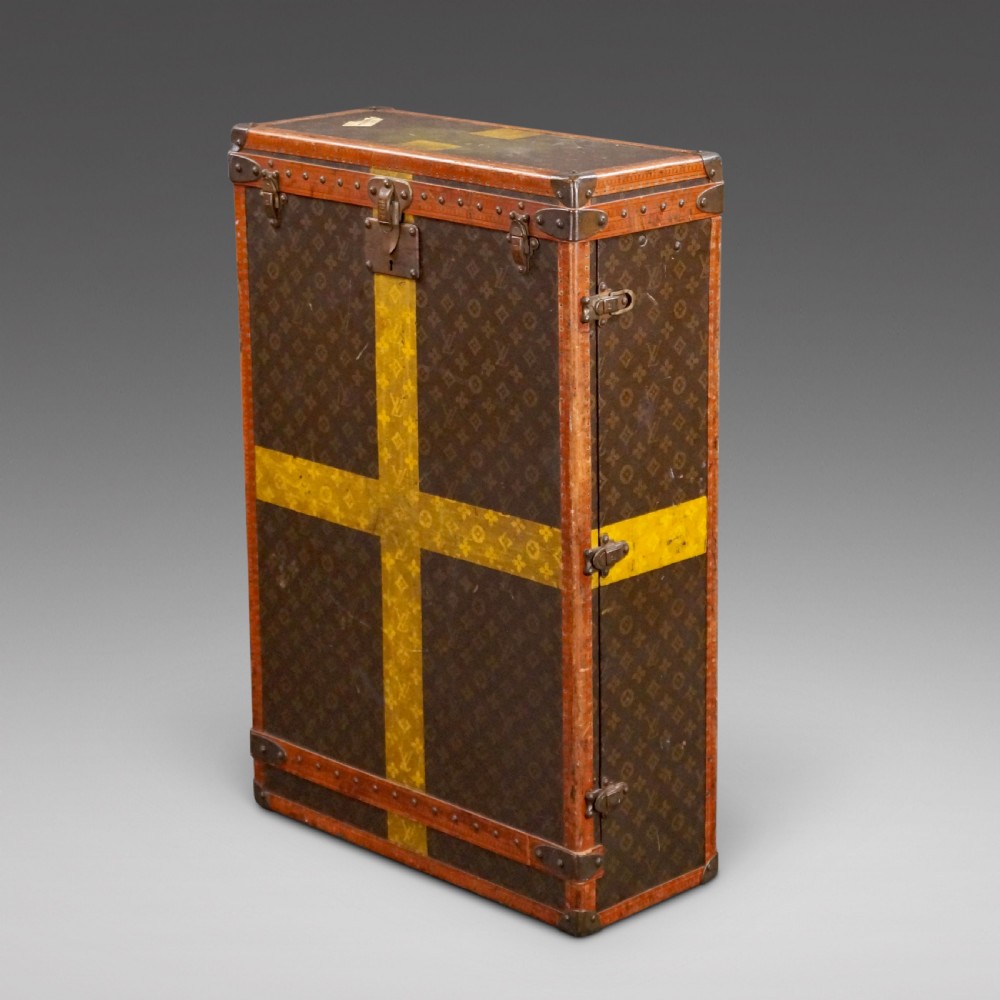 An upright 1930s Louis Vuitton monogram canvas wardrobe trunk featuring leather trim, brass hardware, and custom yellow painted stripes.