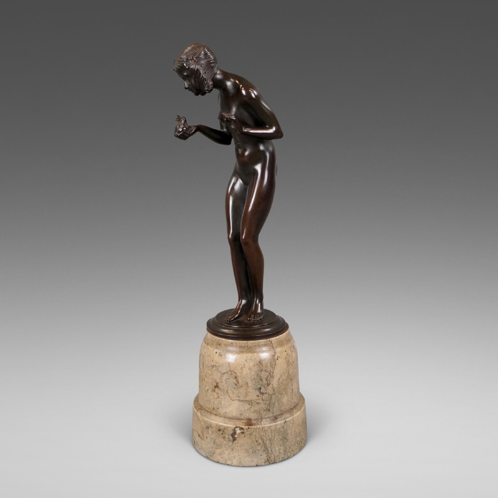 An Art Deco dark bronze sculpture depicting a standing female nude holding a small frog, mounted on a cylindrical veined marble pedestal base.