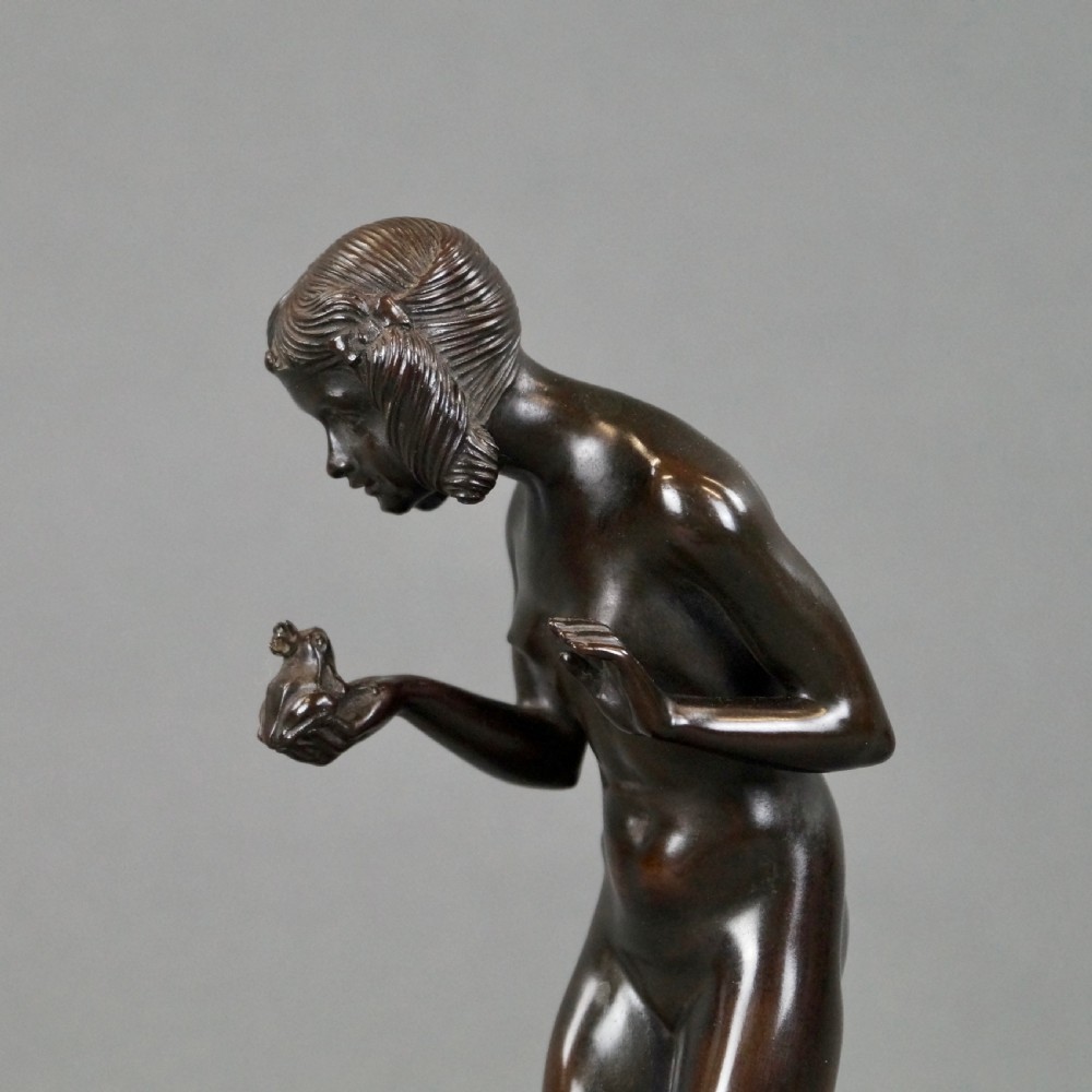 An Art Deco dark bronze sculpture depicting a standing female nude holding a small frog, mounted on a cylindrical veined marble pedestal base. View II