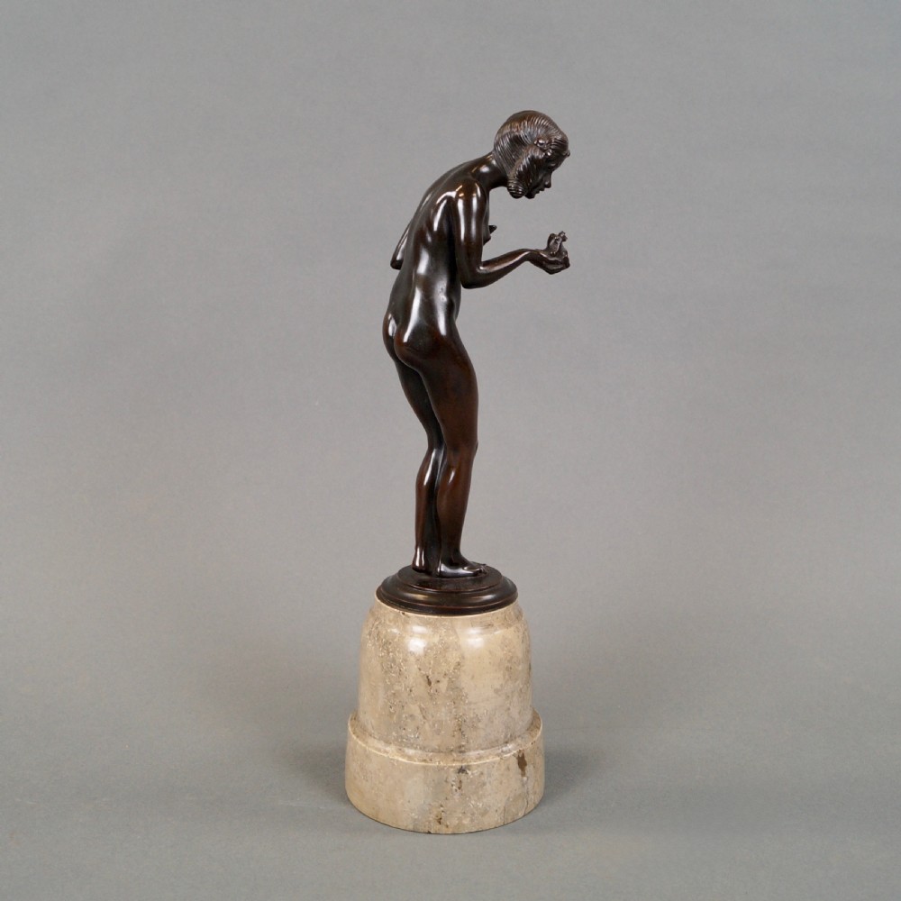 An Art Deco dark bronze sculpture depicting a standing female nude holding a small frog, mounted on a cylindrical veined marble pedestal base. View V