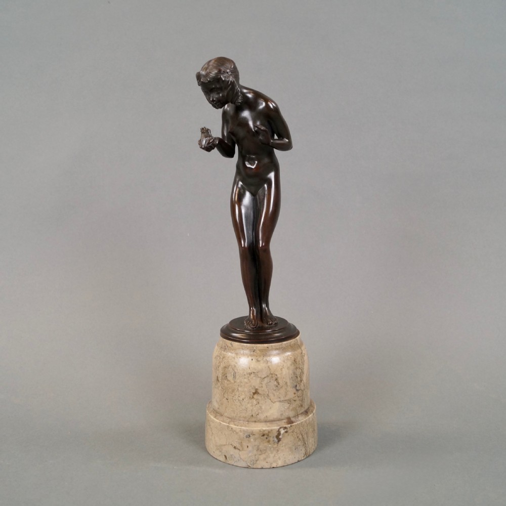 An Art Deco dark bronze sculpture depicting a standing female nude holding a small frog, mounted on a cylindrical veined marble pedestal base. View VI
