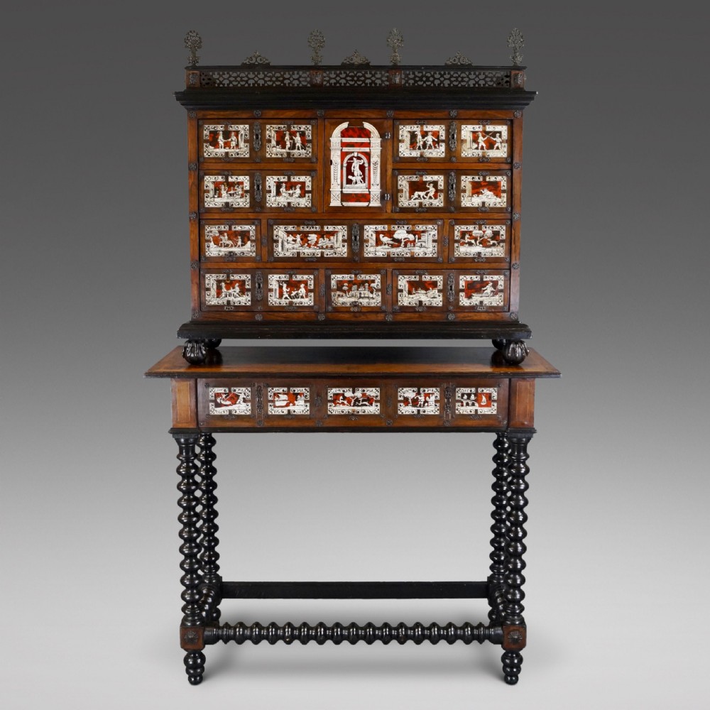 A 19th-century Portuguese cabinet on stand featuring inlaid bone figurative scenes, multiple drawer fronts surrounding a central arch, and a stand supported by dark spiral-turned legs.
